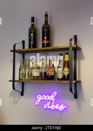 Une belle enseigne rose vif « Good Vibes » néon et une étagère avec des bières sélectionnées sur un mur blanc, accrochées à un joli bar branché, à Milan, en Italie Banque D'Images