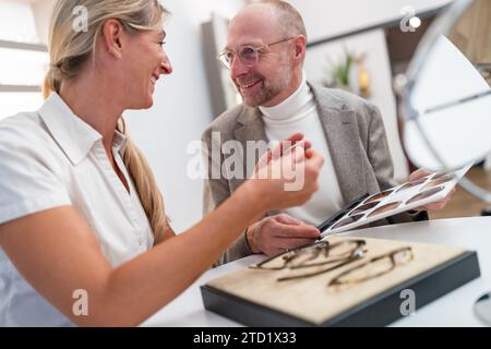 opticien montrant et souriant tout en regardant une sélection de verres de lunettes de soleil dans le magasin optique Banque D'Images