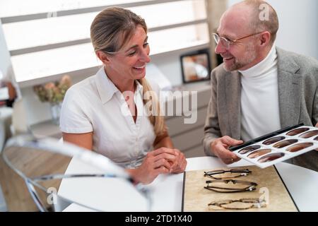 opticien et client souriant et regardant une sélection de verres de lunettes de soleil pour lunettes dans le magasin d'optique. Banque D'Images