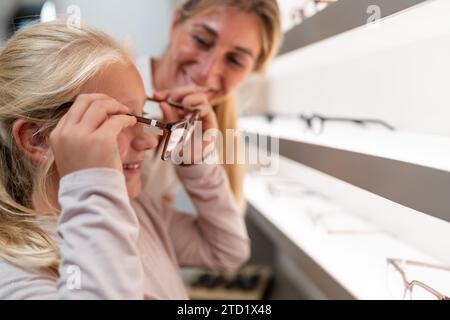 Adulte aider un enfant à essayer de nouvelles lunettes dans un magasin d'optique Banque D'Images