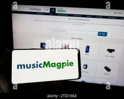 Personne tenant un téléphone mobile avec le logo de la société britannique de commerce électronique MusicMagpie devant la page Web d'affaires. Concentrez-vous sur l'affichage du téléphone. Banque D'Images