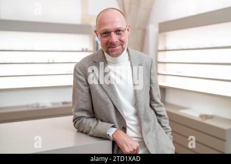 opticien avec des lunettes souriant à la caméra dans un magasin de lunettes. Il porte une veste et un col roulé. Banque D'Images