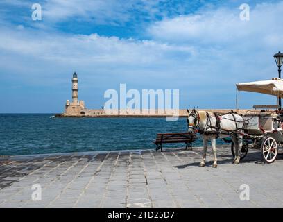 Calèche blanche tirée par des chevaux et phare au port vénitien , Vieille ville de la Canée Crète, Grèce. Moyens de transport traditionnels en bord de mer. Banque D'Images