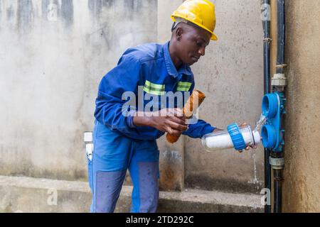 Plombier africain attentif changeant les cartouches d'eau de sale à propre. Banque D'Images