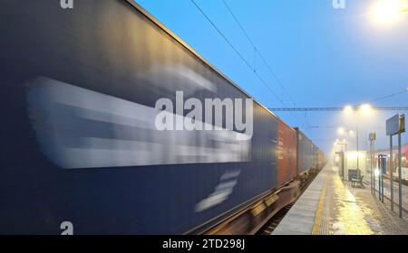 Train de nuit dans le brouillard. Station dans le brouillard et l'obscurité. Passage d'un train de marchandises dans le brouillard et l'obscurité. Concept de problèmes de trafic, train de marchandises en mouvement Banque D'Images