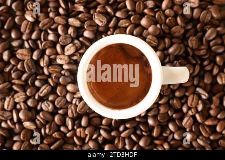 Une vue donnant directement vers le bas sur une tasse à espresso blanche remplie d'une dose de café fraîchement préparée avec de la crème brune. Fond de grains de café torréfiés. Banque D'Images