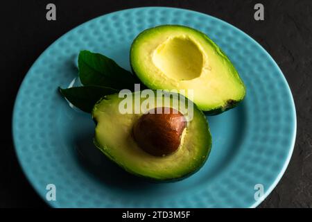 Avocat frais coupé en deux sur une assiette en céramique bleue sur un tableau noir. Concept d'alimentation saine. Photographie culinaire Banque D'Images