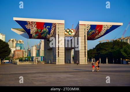 Séoul, Corée du Sud - 2 juin 2023 : les joggeurs du matin traversent la cour du parc olympique, avec la porte mondiale de la paix illuminée par le lever du soleil Banque D'Images