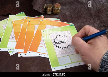 Main masculine choisissant des numéros sur un billet de loterie, sous forme de symbole de devise euro, sur cuir véritable Banque D'Images