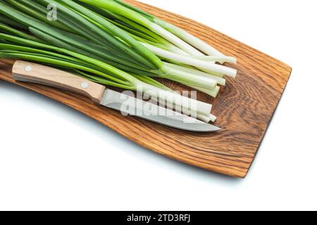 Tiges d'oignons verts de printemps avec couteau de cuisine sur planche à découper en bois isolé blanc Banque D'Images