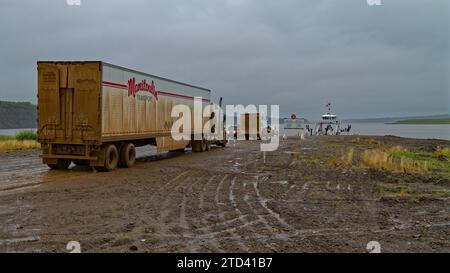 En attendant le traversier au fleuve Mackenzie, camion sale et plusieurs voitures sur la route boueuse Dempster en face, fleuve Mackenzie et traversier visibles Banque D'Images