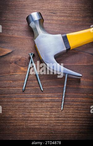 Marteau à griffes avec manche jaune et clous sur une vieille planche de bois Banque D'Images