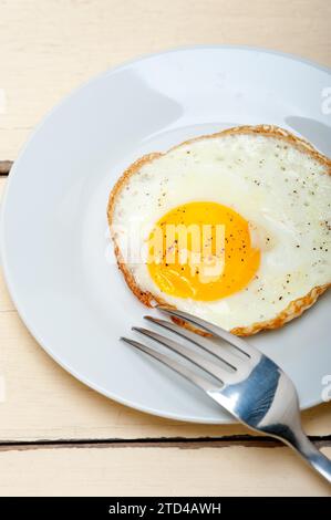 Oeuf frit côté ensoleillé vers le haut sur une assiette avec fourchette au-dessus de la table en bois Banque D'Images