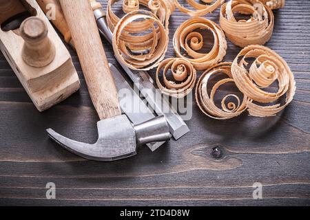 Image rapprochée de burin en métal de marteau de pince raboteuse et copeaux de bois frisés sur le concept de construction de planche en bois vintage Banque D'Images