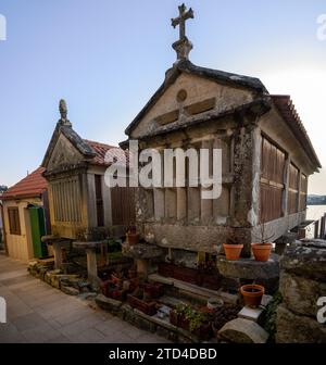 Greniers traditionnels en pierre (horreos) à Combarro, Galice, Espagne, avec des plantes en pot et une croix sur le toit, près de la mer. Banque D'Images