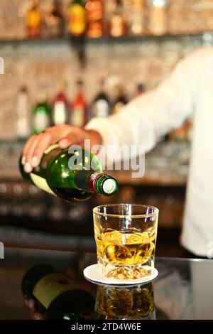 Un barman mâle versant un verre de whisky dans un pub Banque D'Images