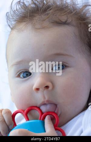 Adorable petit bébé de 4 mois tenant jouet anneau de dentition près du mois. Visage de bébé. Fond blanc. Banque D'Images