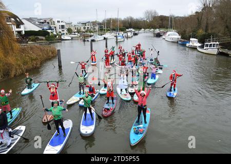 Groupe de paddle boarders habillés en Père Noël et Elfes. Événement de Noël organisé par les BH Activity Junkies sur la rivière Stour à Christchurch Dorset Royaume-Uni Banque D'Images