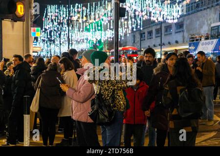 Londres, Royaume-Uni. 16 décembre 2023. Les gens admirent les lumières de Noël dans Oxford Street et prennent des photos. L'avant-dernier samedi précédant Noël, le West End regorge de clients et de touristes. Les détaillants ont fait une dernière tentative pour stimuler les ventes. Le British Retail Consortium (BRC) a rapporté le mois dernier que les magasins étaient confrontés à un « Noël difficile », les consommateurs dépensant moins. Crédit : Photographie de onzième heure / Alamy Live News Banque D'Images