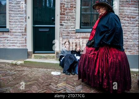 Deventer, pays-Bas . 16 décembre 2023. Deux petites filles sont assises sur le sol et se produisent comme des sans-abri. Chaque année, vers cette date, le monde du 19e siècle de l'écrivain anglais Charles Dickens revit dans la belle ville hollandaise de Deventer. Plus de 950 personnages des célèbres livres de Dickens remontent à la vie. Riches dames et messieurs avec des chapeaux de haut défilé dans les rues.le paysage du festival se compose de bâtiments historiques, arbres de Noël, et des milliers de petites lumières. Crédit : SOPA Images Limited/Alamy Live News Banque D'Images