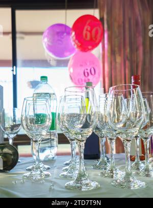 ballons du 60e anniversaire suspendus à la fenêtre, focalisation sélective sur les verres à vin sur la table. Fête d'anniversaire. Format vertical. Banque D'Images