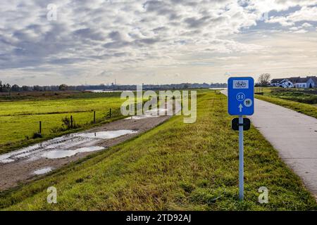 Piste cyclable dans la réserve naturelle belge de Wissen, entre un sentier de randonnée avec flaques d'eau et campagne, fermes en arrière-plan, routes 50 et 19, journée nuageuse Banque D'Images