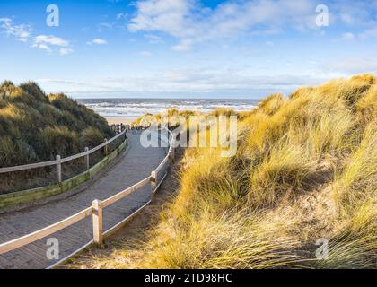 Un panorama multi-images d'une promenade en planche incurvée serrant à travers les dunes de sable menant à la magnifique plage et la côte à Formby près de Liverpool. Banque D'Images