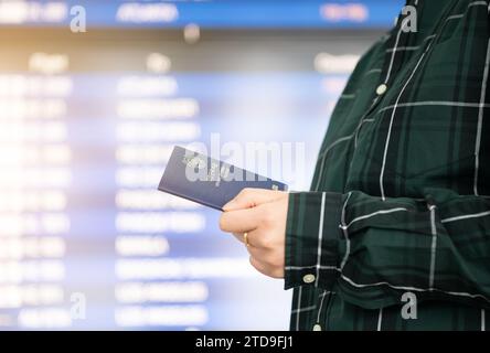 Une femme passant devant un tableau d'information sur les horaires de l'aéroport avec son passeport en main Banque D'Images