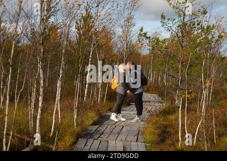 Les touristes avec des sacs à dos embrassent un chemin en bois dans un marais à Yelnya, Biélorussie. Banque D'Images