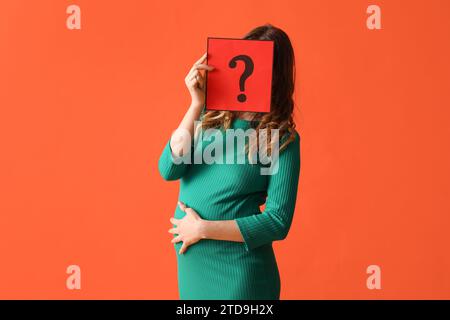 Jeune femme enceinte tenant une feuille de papier avec un point d'interrogation sur fond orange Banque D'Images