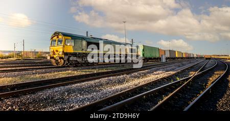 Vue de profil d'un train de marchandises avec des wagons intermodaux remplis de boîtes de conteneurs d'expédition pour l'importation et l'exportation dans une cour de triage ou des voies d'évitement Banque D'Images