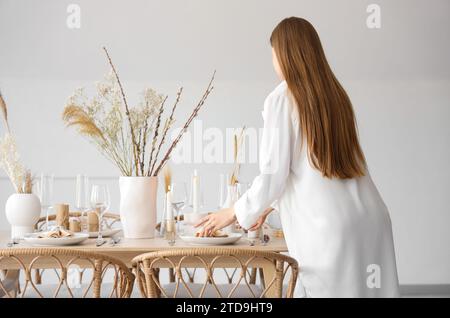 Belle femme mettant table avec des fleurs séchées dans la salle à manger Banque D'Images