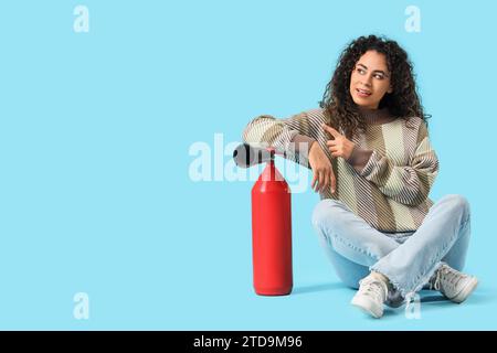 Jeune femme afro-américaine avec extincteur pointant quelque chose sur fond bleu Banque D'Images