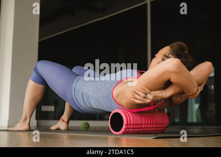 Fille mince faisant du yoga avec un gros rouleau de massage sur le sol. Banque D'Images