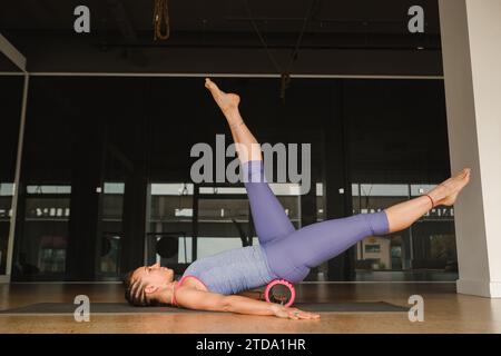 Fille mince faisant du yoga avec un gros rouleau de massage sur le sol. Banque D'Images