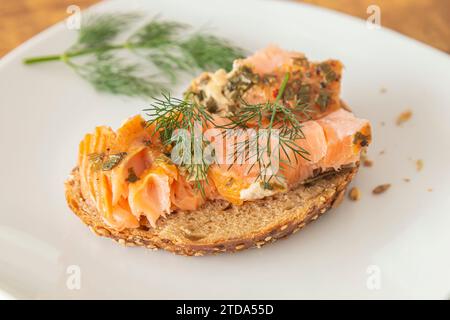 Un morceau de pain frais avec du saumon fumé et une branche d'aneth sur une assiette blanche. Gros plan. Banque D'Images