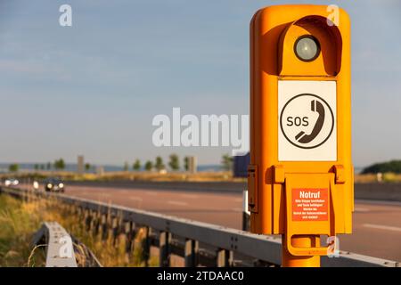 Sécurité routière : Orange boîte d'appel SOS sur l'autoroute allemande au milieu des feux de voiture floues, Traduction de texte allemand : SOS, appel d'urgence, s'il vous plaît soulever le volet Banque D'Images