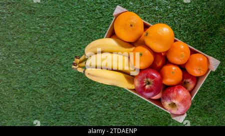 caisse de fruits en bois sur l'herbe avec différents fruits pomme orange banane et mandarine Banque D'Images