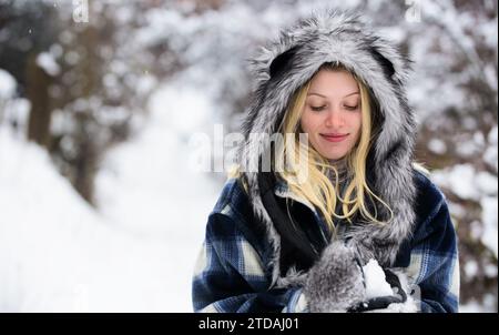 Jolie femme dans des vêtements élégants avec boule de neige dans les mains. Fille souriante en tenue chaude jouant avec la neige dans le parc d'hiver. Belle femme en manteau écossais Banque D'Images