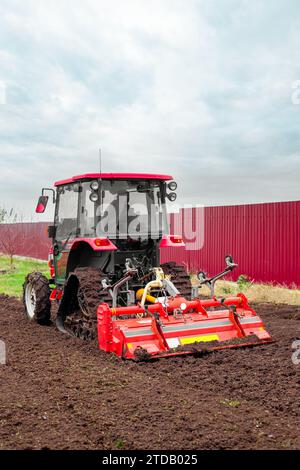 un tracteur caterpillar équipé d'une débroussailleuse aspire le sol d'un terrain de jardin. Banque D'Images