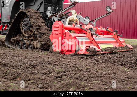 un tracteur caterpillar équipé d'une débroussailleuse aspire le sol d'un terrain de jardin. Banque D'Images