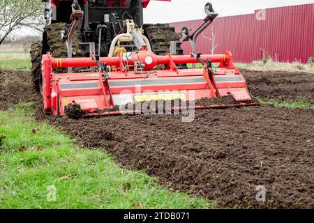 un tracteur caterpillar équipé d'une débroussailleuse aspire le sol d'un terrain de jardin. Banque D'Images