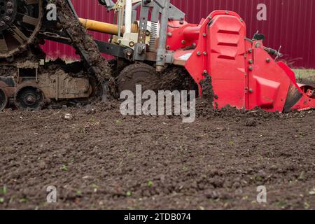 un tracteur caterpillar équipé d'une débroussailleuse aspire le sol d'un terrain de jardin. Banque D'Images