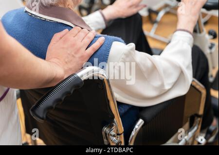 Gros plan l'infirmière touche l'épaule d'une patiente âgée en fauteuil roulant la soutenant en montrant de l'empathie et de la compassion, en se souciant du concept des personnes âgées. Photographie de haute qualité Banque D'Images
