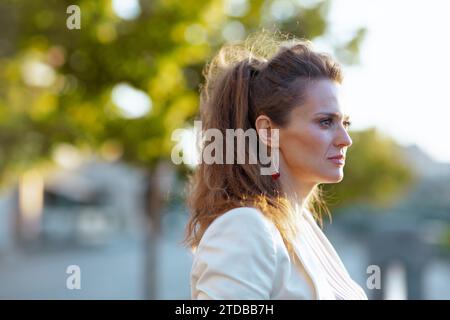 pensive tendance femme de 40 ans en robe rose et veste blanche dans la ville regardant dans la distance. Banque D'Images