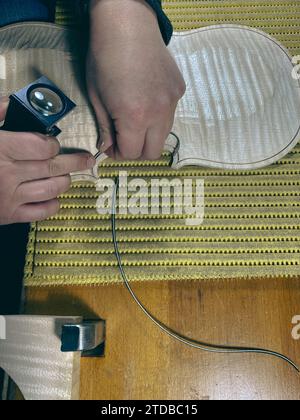 violoniste effectuant un ronflage sur une nouvelle plaque supérieure de violon brute à l'aide d'une loupe pour vérifier l'image haute résolution du canal incrusté Banque D'Images