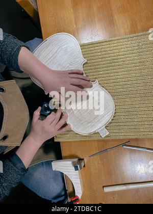 violoniste effectuant un ronflage sur une nouvelle plaque supérieure de violon brute à l'aide d'une loupe pour vérifier l'image haute résolution du canal incrusté Banque D'Images