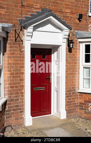 Maison de ville traditionnelle typiquement anglaise en briques géorgiennes avec un porche géorgien blanc de type ouvert et une porte d'entrée rouge. New Alresford, Angleterre Banque D'Images