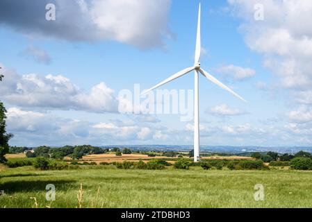 Grande éolienne dans un paysage rural vallonné sur une journée ensoleillée d'été. Une ville est visible en arrière-plan. Banque D'Images