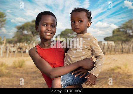 Famille, filles africaines à la ferme, kraal avec des chèvres en arrière-plan, Kalahari petit bétail dans le village Banque D'Images